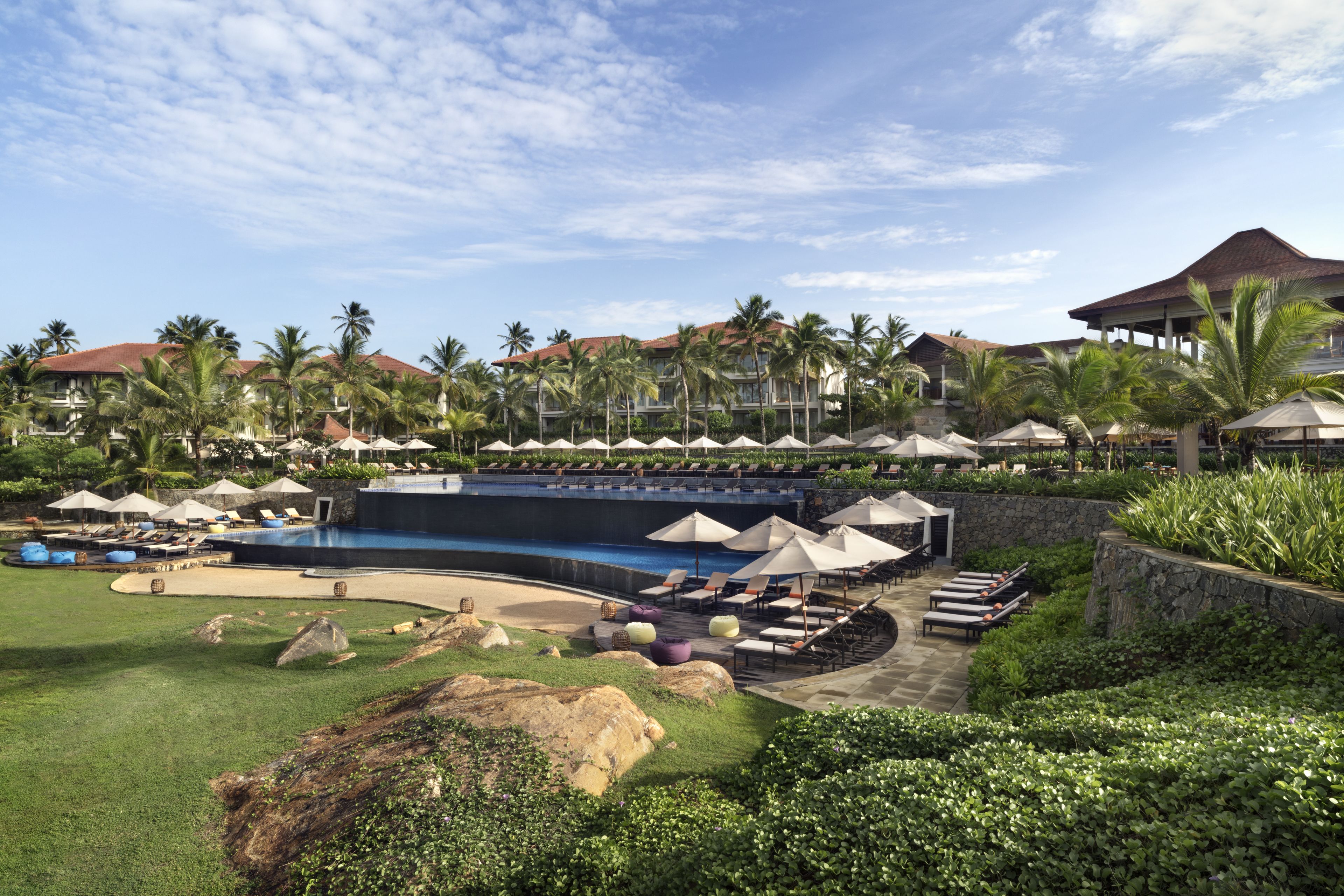 Un resort con piscina, sillas de descanso, sombrillas y palmeras.