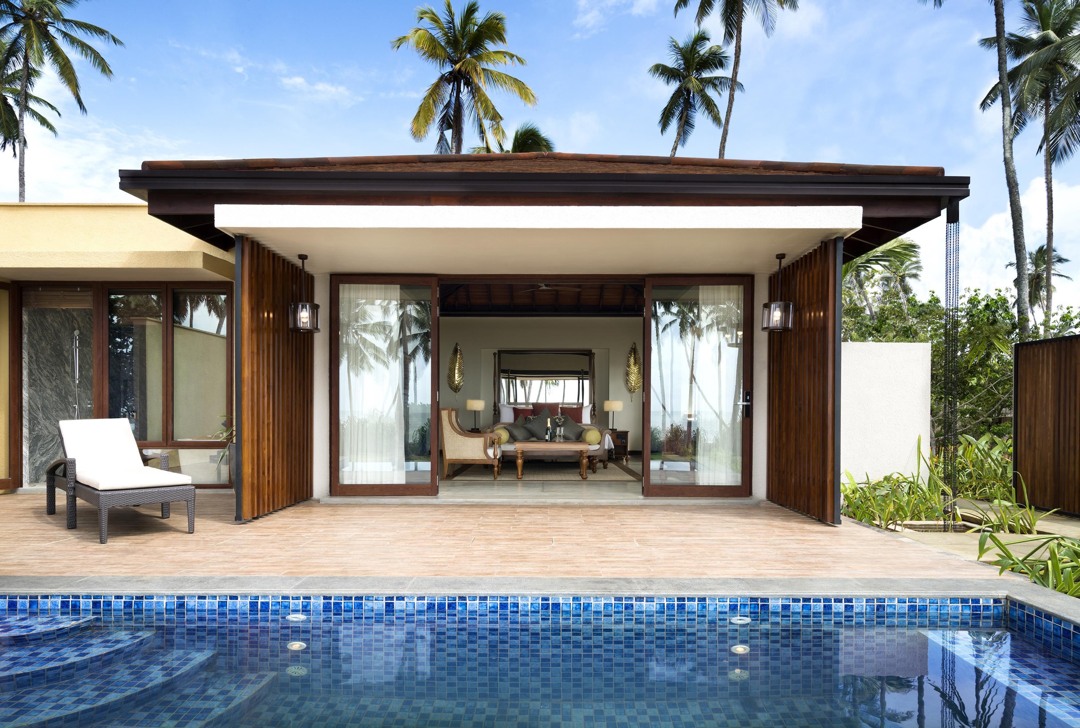 A modern poolside area with a lounge chair, a sofa set, and a view of the pool.
