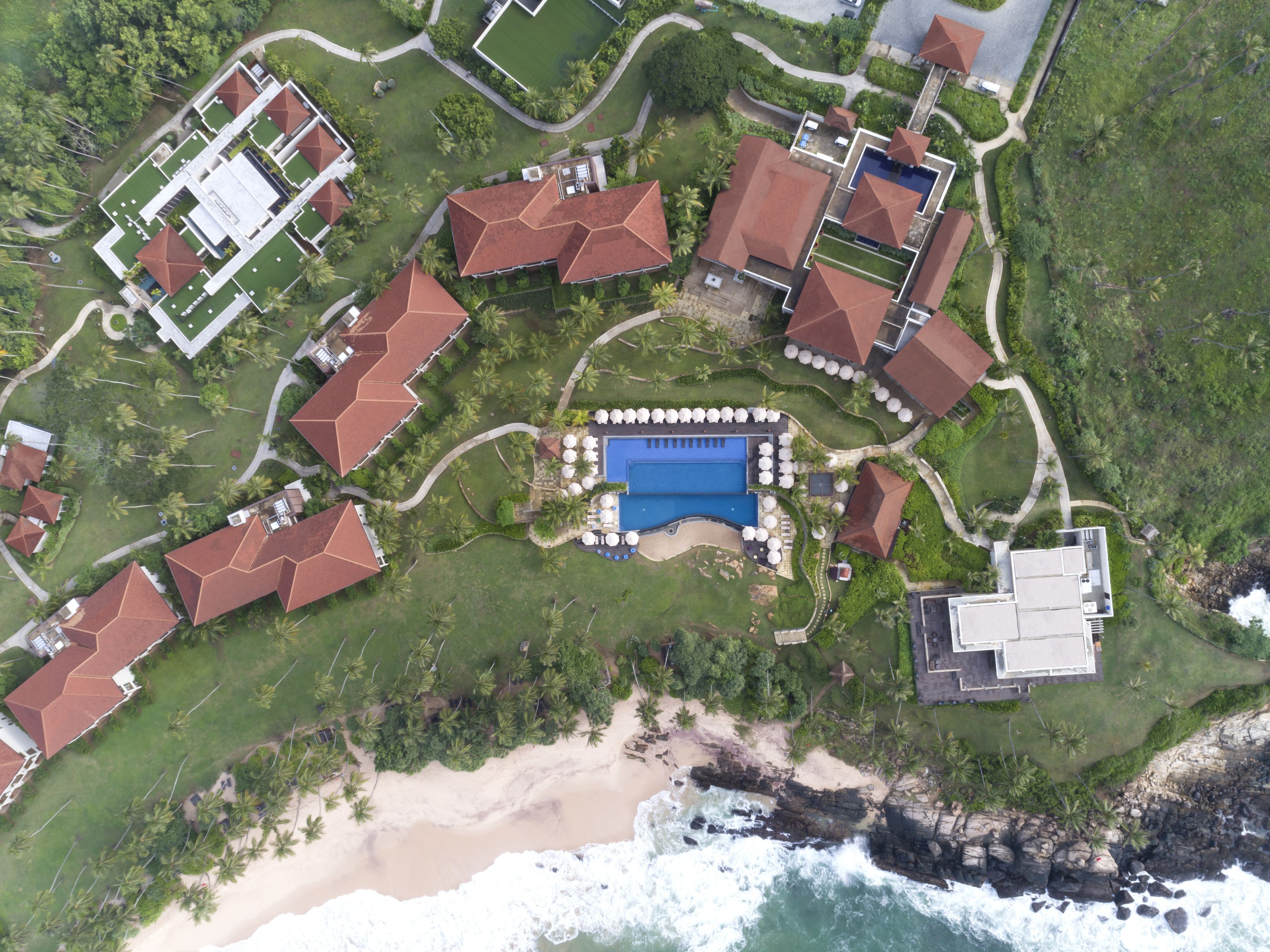 An aerial view of a resort with multiple buildings, a central swimming pool, and a beach area.