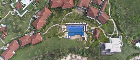 An aerial view of a resort with multiple buildings, a central swimming pool, and a beach area.