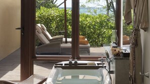Une salle de bain moderne avec une baignoire, une chaise en bois et une vue sur une piscine et la verdure.