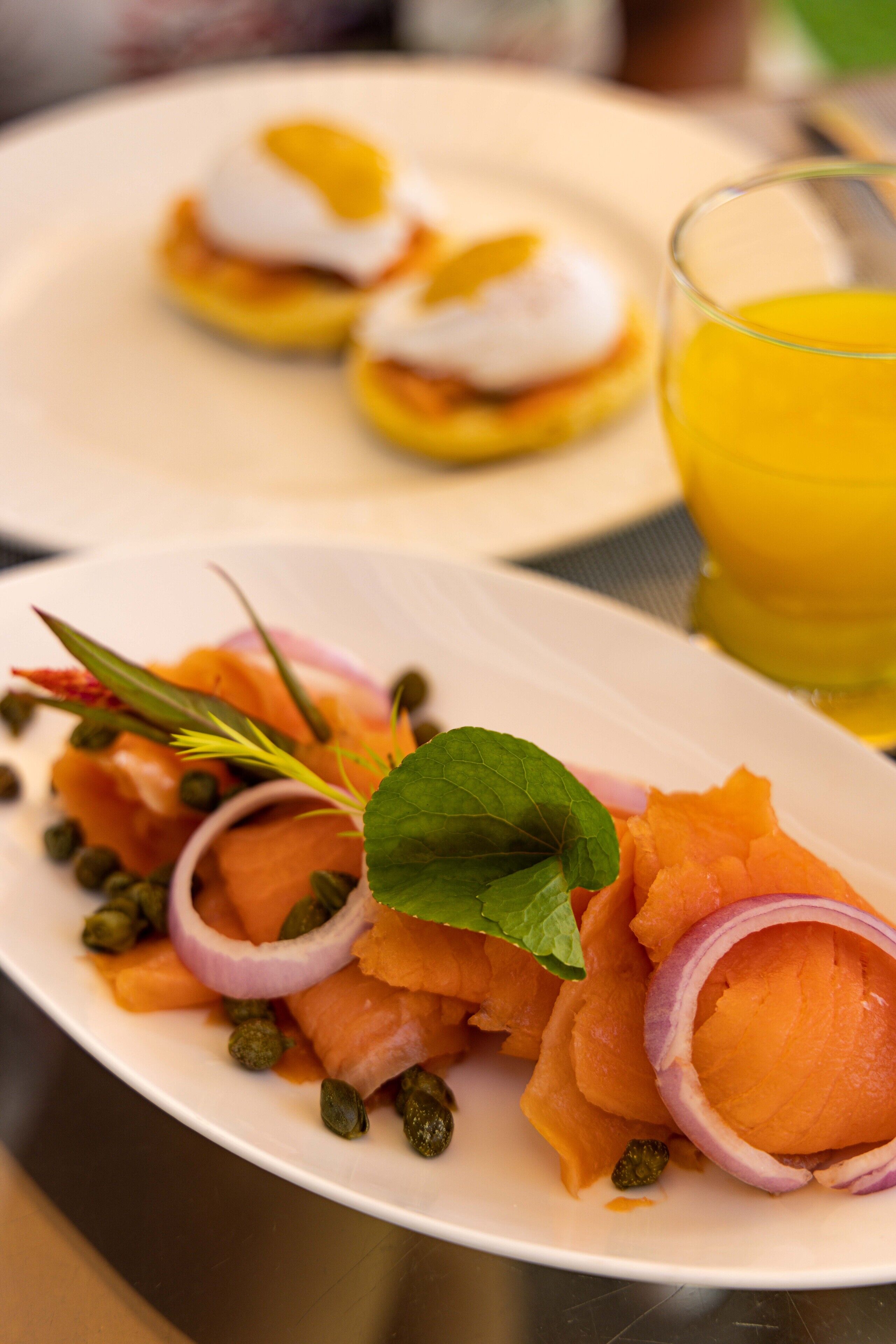 A plate of smoked salmon with capers, red onion, and a sprig of herb.