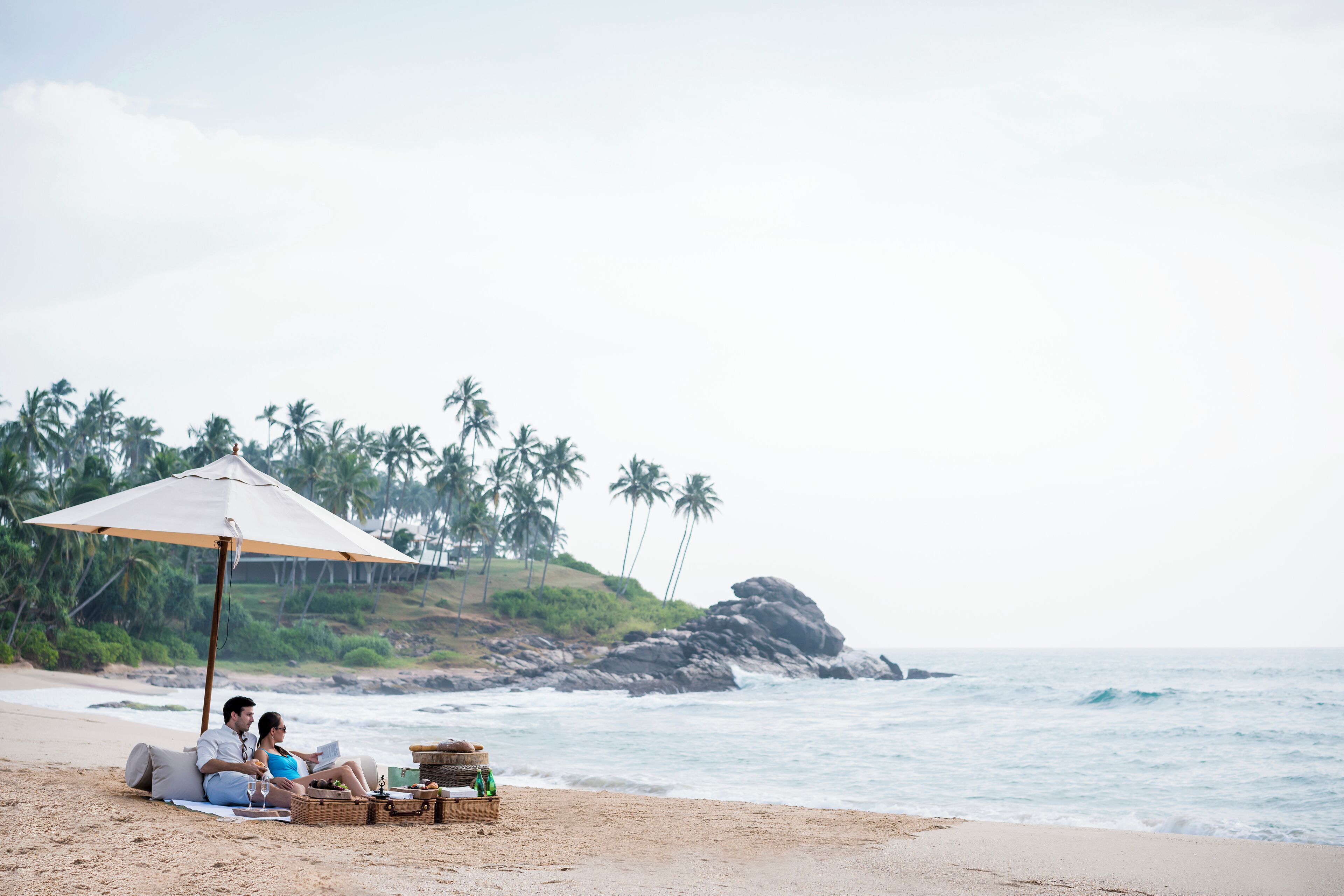 A couple relaxing on a beach with an umbrella, surrounded by beachside amenities.