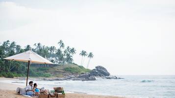 A couple relaxing on a beach with an umbrella, surrounded by beachside amenities.
