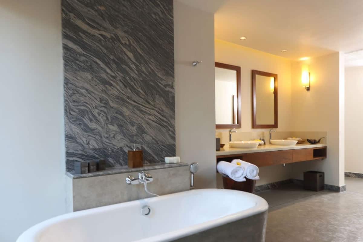 Un baño moderno con una bañera independiente, una pared de mármol, un espejo grande y un tocador con lavamanos y toallero.