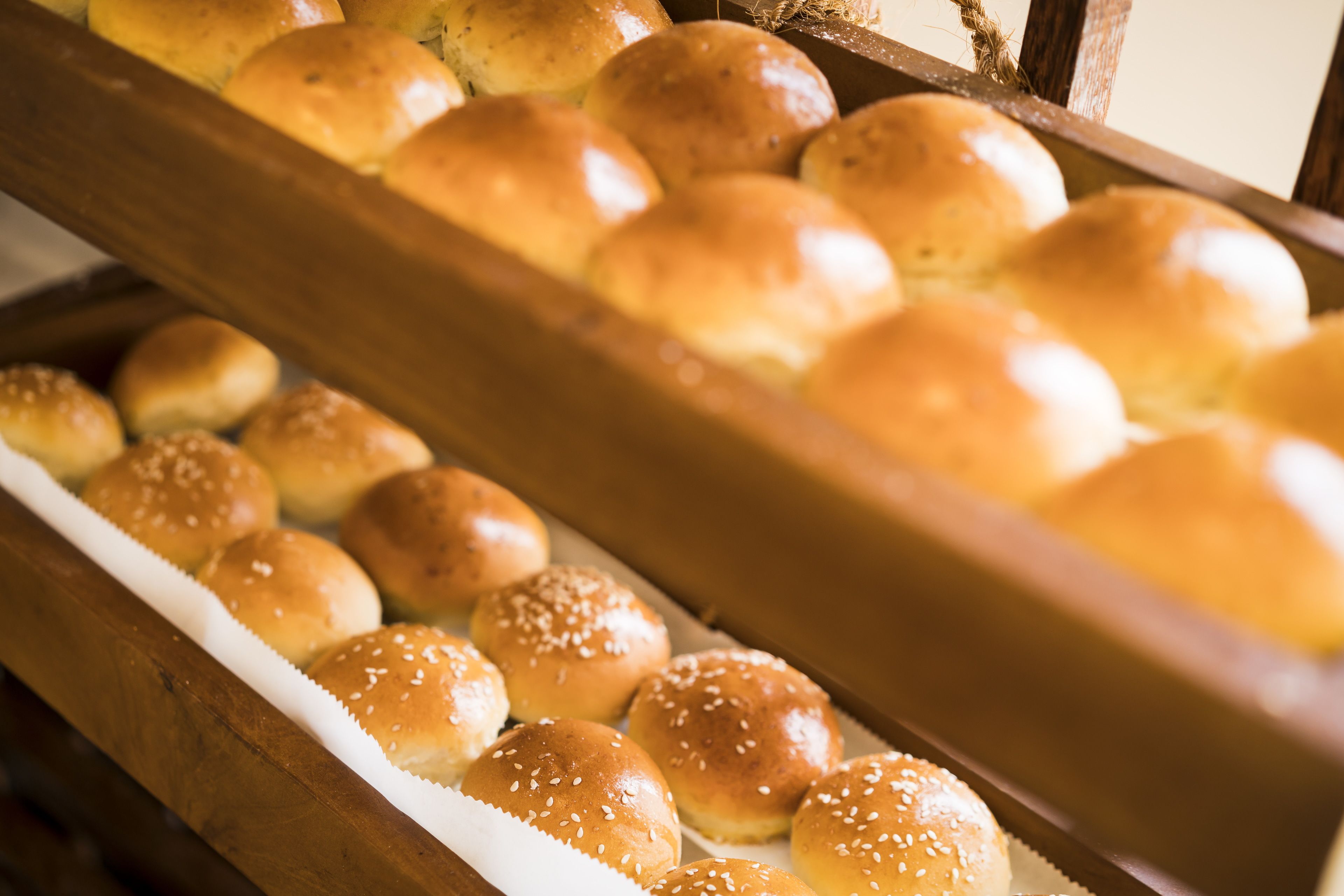 A wooden tray with various types of bread rolls, including some with sesame seeds.