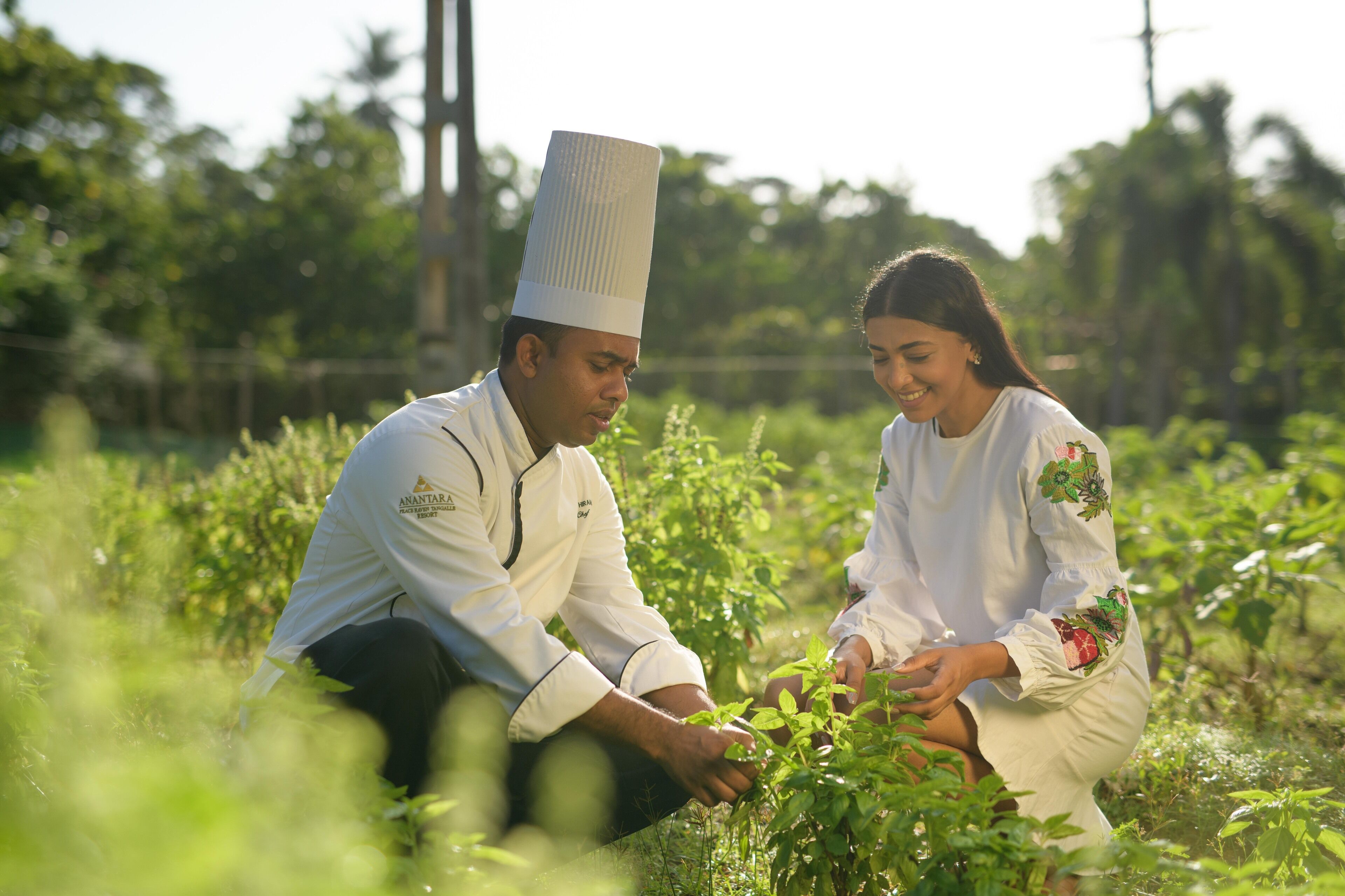 Due persone in un campo, una con cappello da chef e l'altra in un abito bianco con ricami floreali.