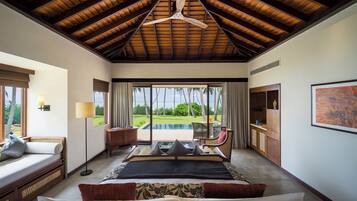 A spacious bedroom with a large bed, a ceiling fan, a view of the pool, and a seating area with a table and chairs.
