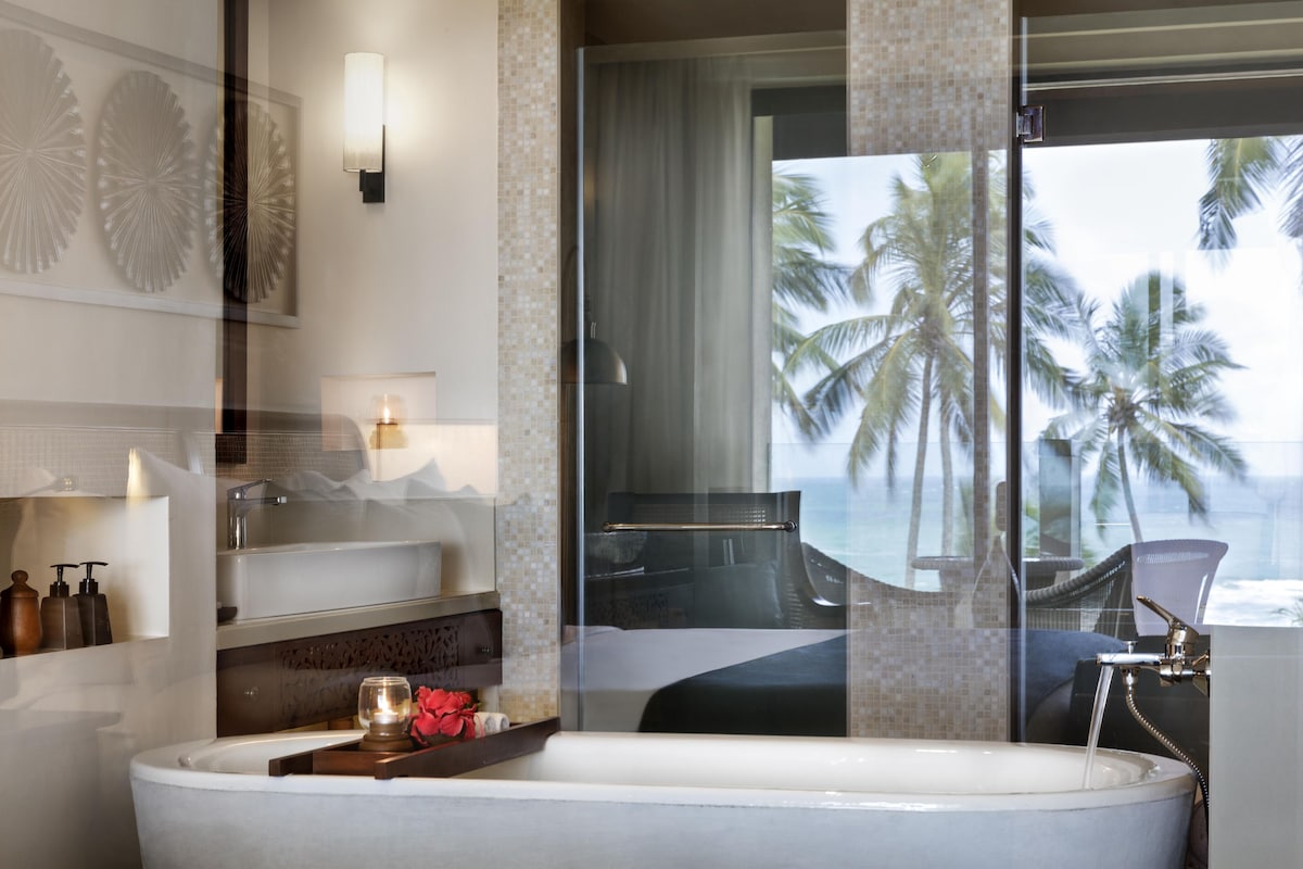 Un baño moderno con bañera, cabina de ducha de vidrio y vistas a palmeras.