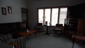 A living room with a sofa, chairs, a coffee table, a TV, and a window with blinds. - Augusta House (Galena)