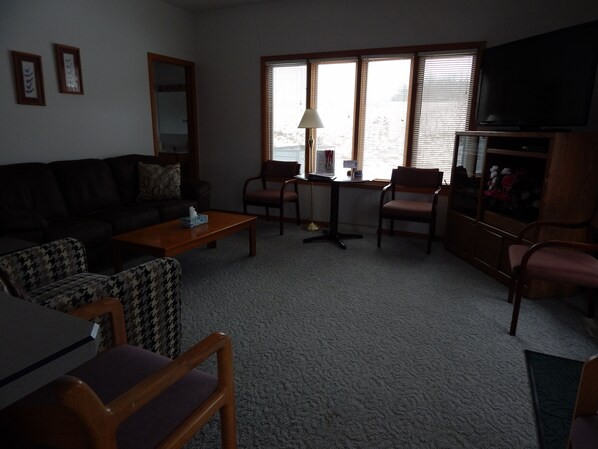 A living room with a sofa, chairs, a coffee table, a TV, and a window with blinds. - Augusta House (Galena)