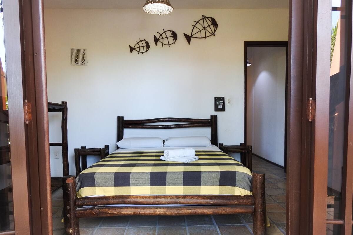 A neatly made bed with a checkered bedspread, wooden headboard, and a towel on the bed. There are three wall-mounted fish decorations and a thermostat on the wall.