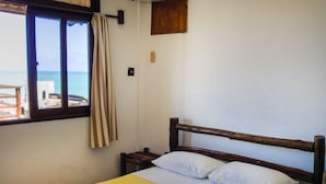 A bed with a yellow bedspread, white pillows, and a rolled towel. There is a window with curtains, a wooden headboard, and a small wooden shelf above the bed. - Apart Hotel Casa Grande (Natal)