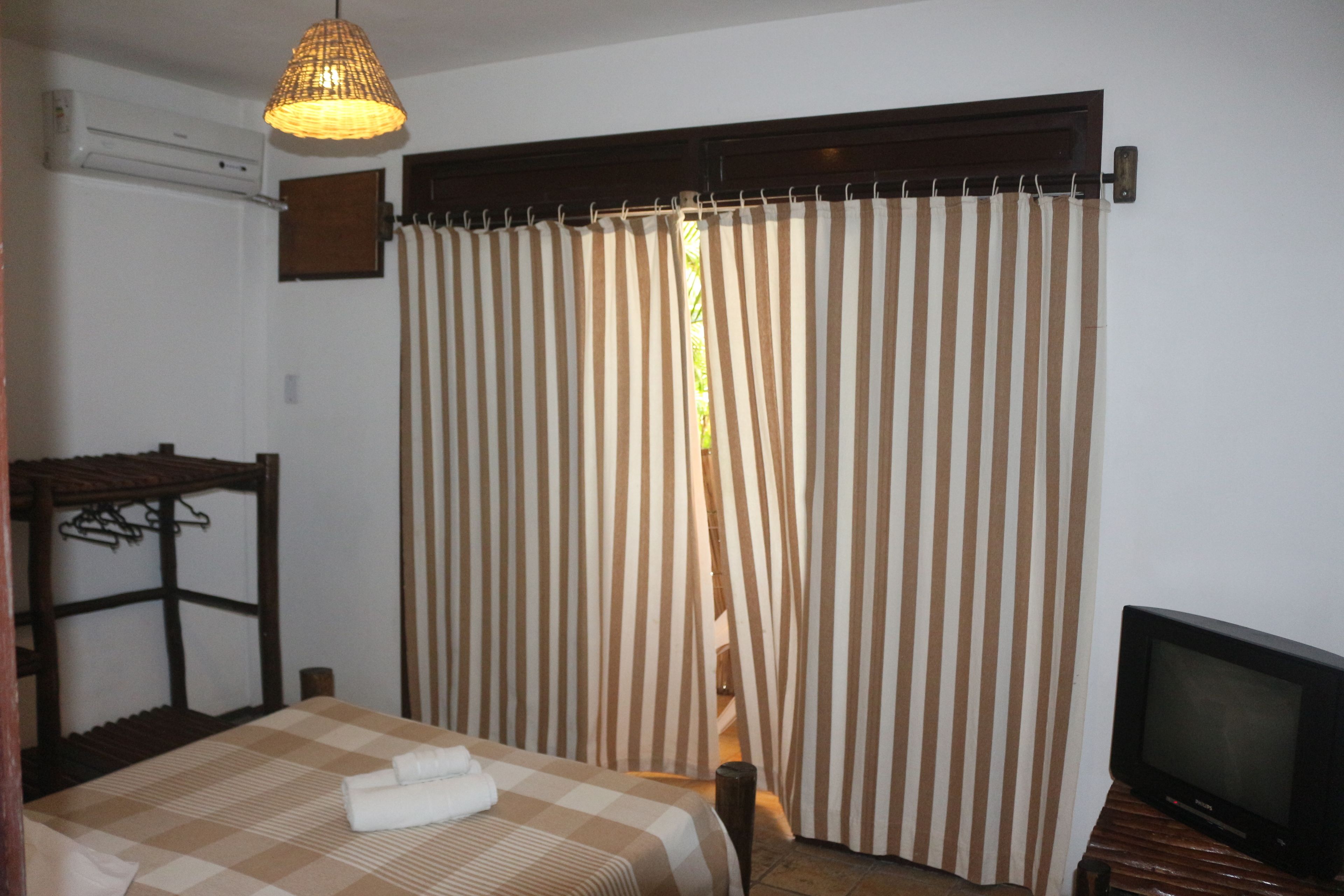 Ein Hotelzimmer mit Bett, Fernseher, einer Pendelleuchte und einem Fenster mit gestreifteren Vorhängen.