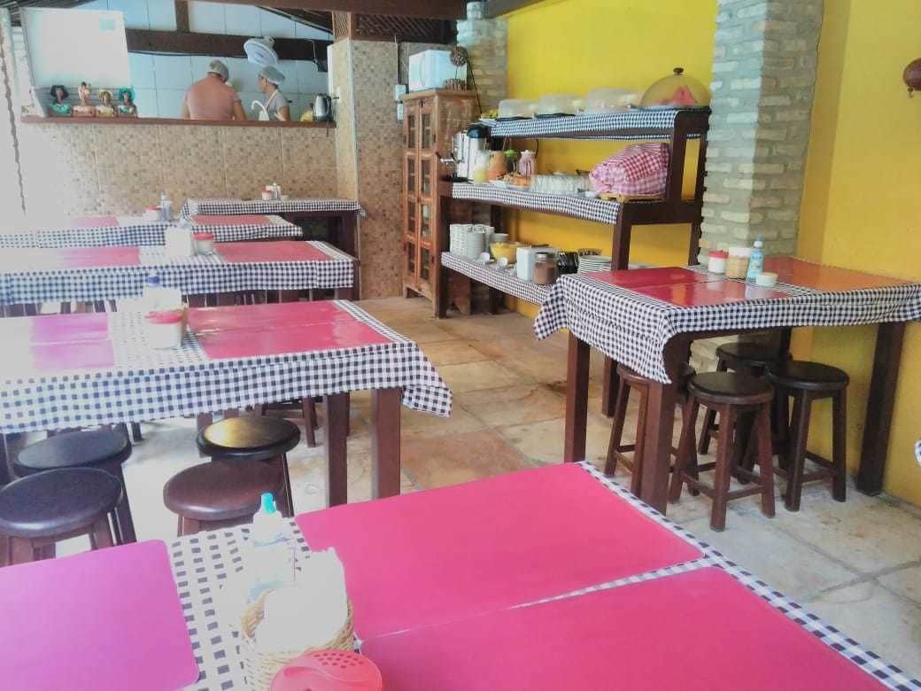A restaurant with checkered tablecloths and red table tops, wooden chairs, and a counter with kitchen items.