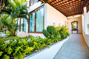 A covered outdoor area with a tiled floor, a white planter with various plants, and a large window with curtains. - Moriah Natal Beach Hotel (Natal)