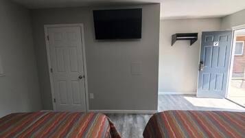 Habitación de hotel con dos camas, un televisor montado en la pared y una puerta que da al exterior.