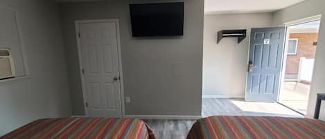 A hotel room with two beds, a television mounted on the wall, and a door leading to the outside.