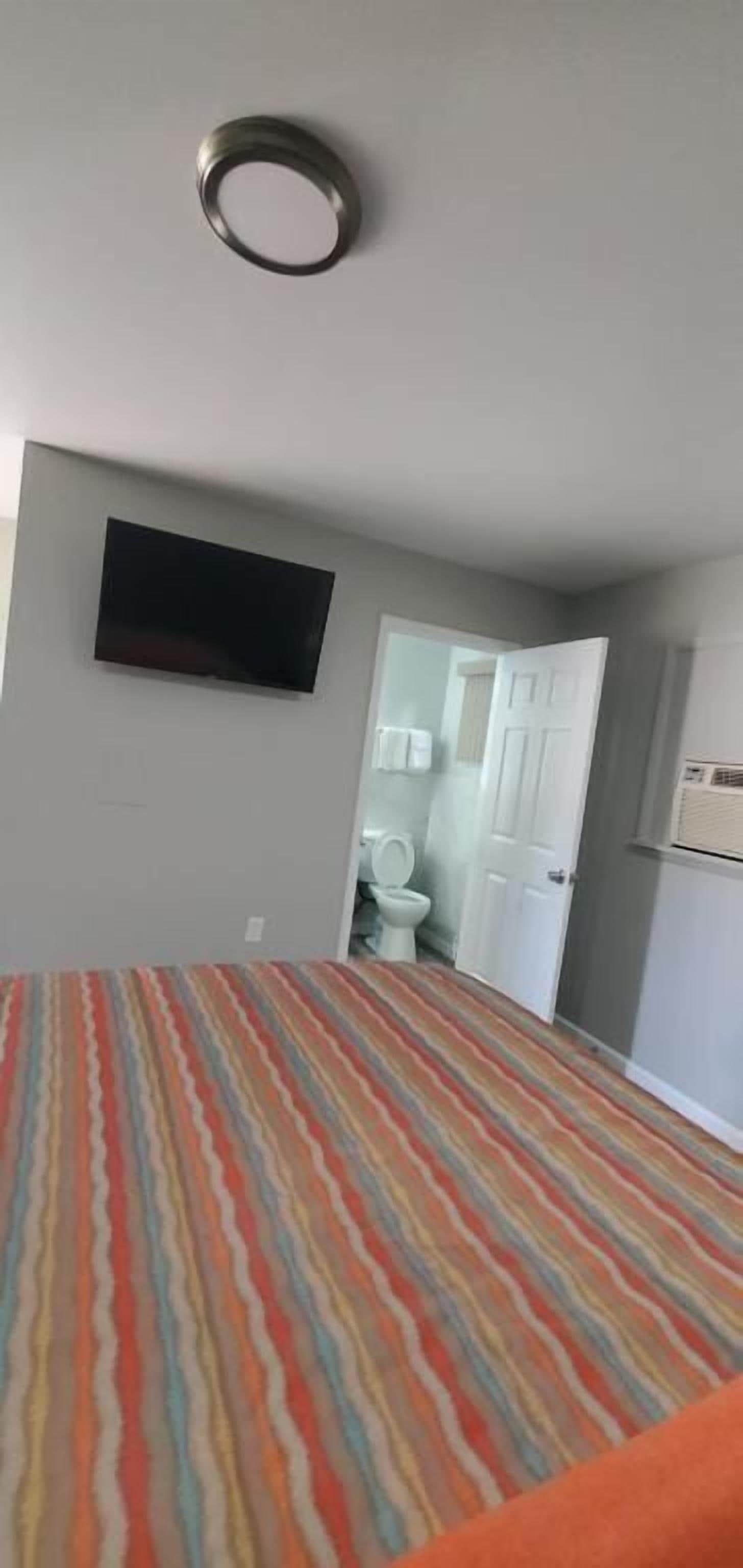 A room with a patterned carpet, a television mounted on the wall, and a door leading to a bathroom.