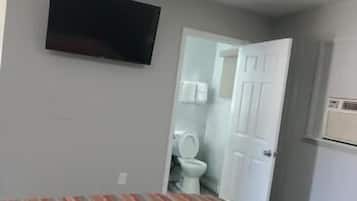 A room with a patterned carpet, a television mounted on the wall, and a door leading to a bathroom.
