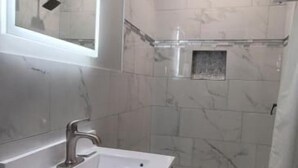 A bathroom with a vanity, sink, mirror, shower, and tiled walls.