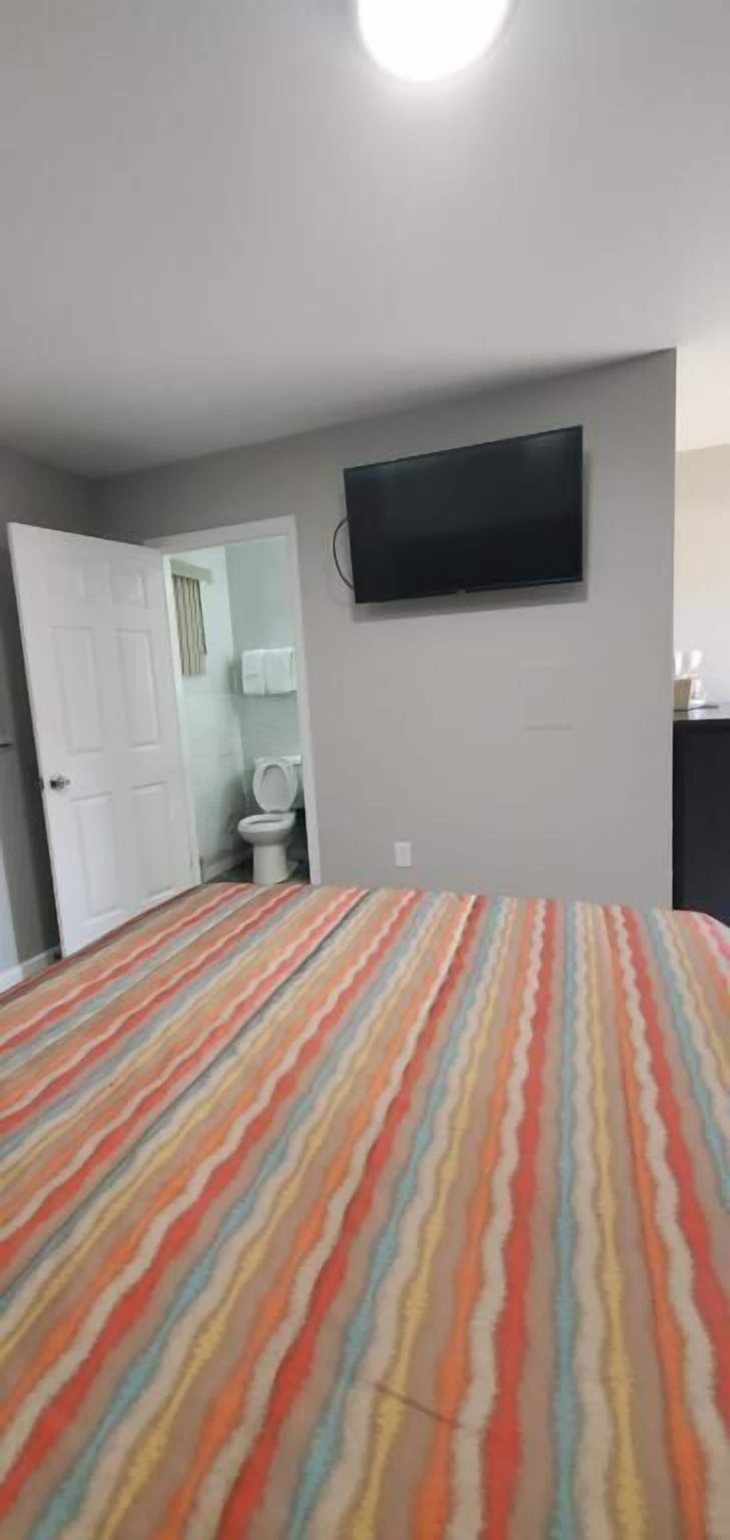 Een slaapkamer met een gestreept beddegoed, een aan de muur bevestigde televisie en een deur naar een badkamer.