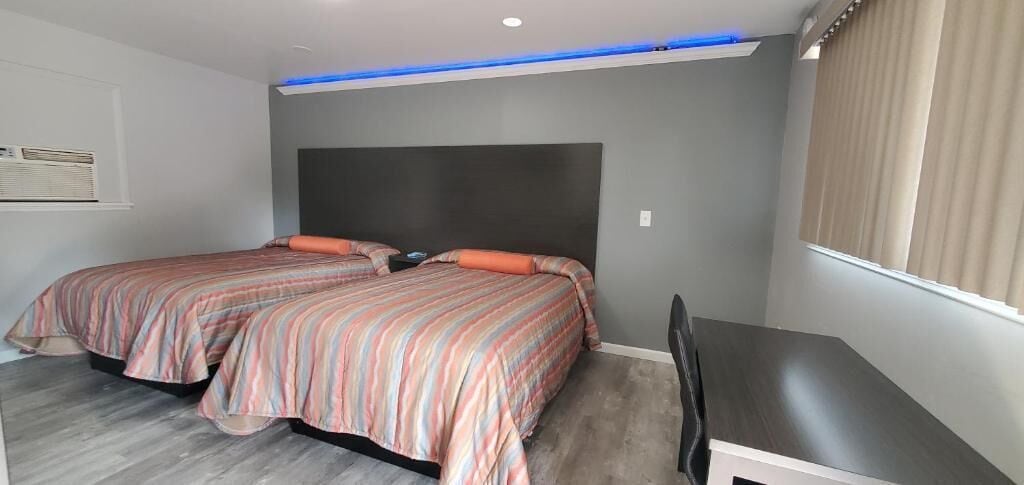 Un dormitorio con dos camas, un escritorio y un ventanal con cortinas.