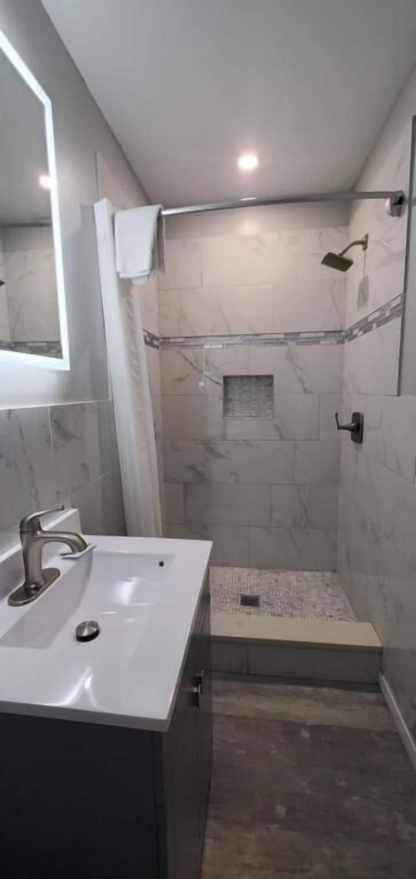 A bathroom with a sink, mirror, shower, and tiled walls.