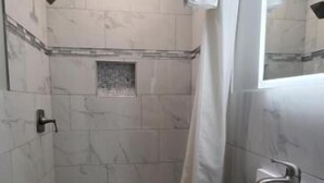 A modern bathroom with a walk-in shower, a sink with a mirror, and a shower curtain. - Villa Rosa Motel (Painesville)