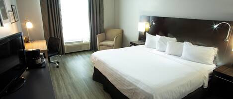 A hotel room with a large bed, a desk with a computer, a chair, and a lamp.