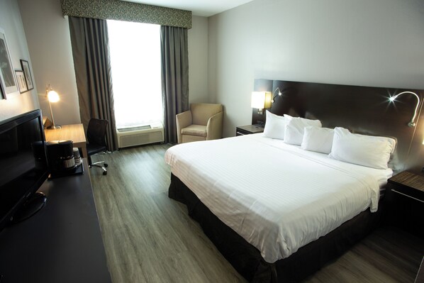 A hotel room with a large bed, a desk with a computer, a chair, and a lamp.
