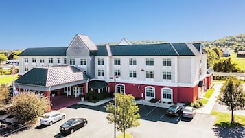 A large hotel with a red and white facade, multiple windows, and a green roof. There is a parking lot with several cars.