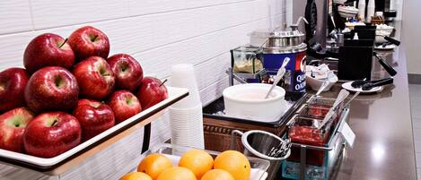 A buffet with apples and oranges, a coffee machine, and various food containers.
