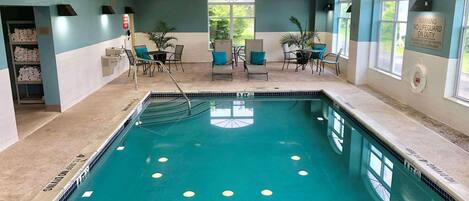 Una piscina interior con una silla de socorrista, sillas junto a la piscina y una mesa con sillas.