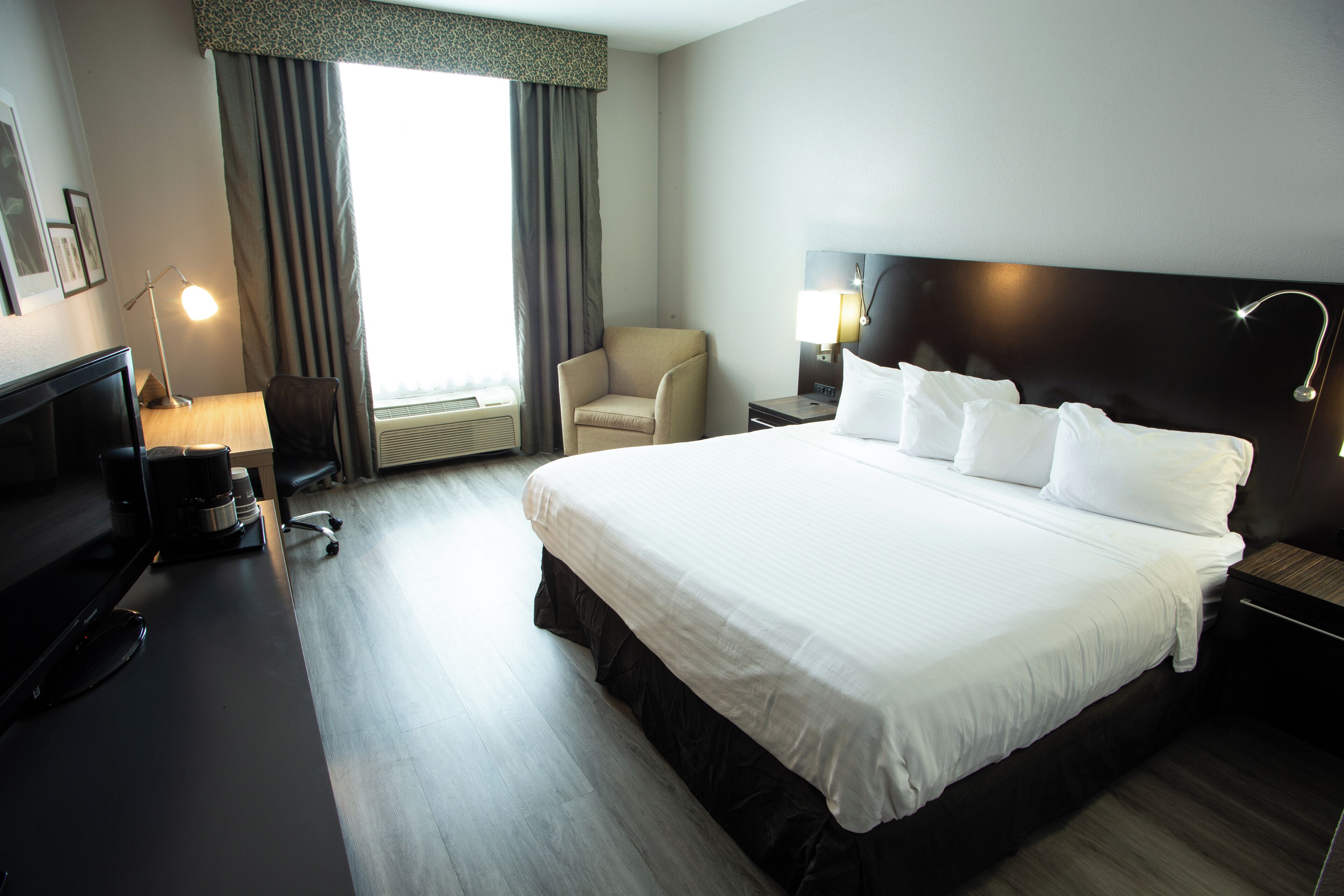 Une chambre d’hôtel avec un grand lit, un bureau avec un ordinateur, une chaise et une fenêtre avec des rideaux.