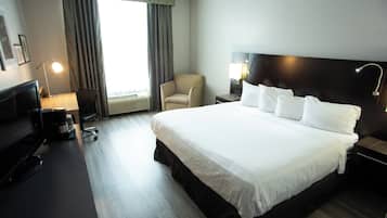 A hotel room with a large bed, a desk with a computer, a chair, and a window with curtains.