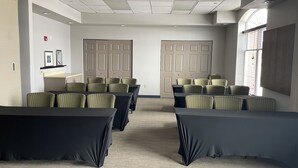 A conference room with tables and chairs, a carpeted floor, and a large window with blinds.