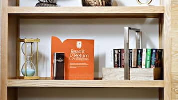 Una estantería con varios libros, objetos decorativos y un folleto que dice 'Read it & Return'.