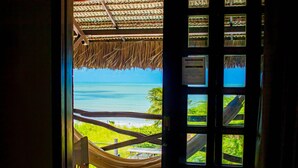 Blick durch ein Fenster mit einem Strohdach und einer Hängematte auf einen Strand und das Meer.