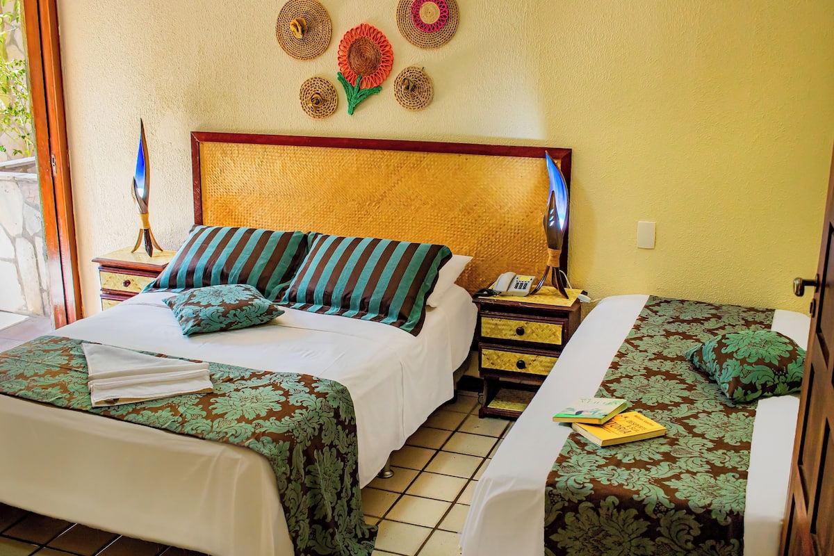 A hotel room with two beds, a wooden headboard, a nightstand with a phone and books, and decorative wall art.