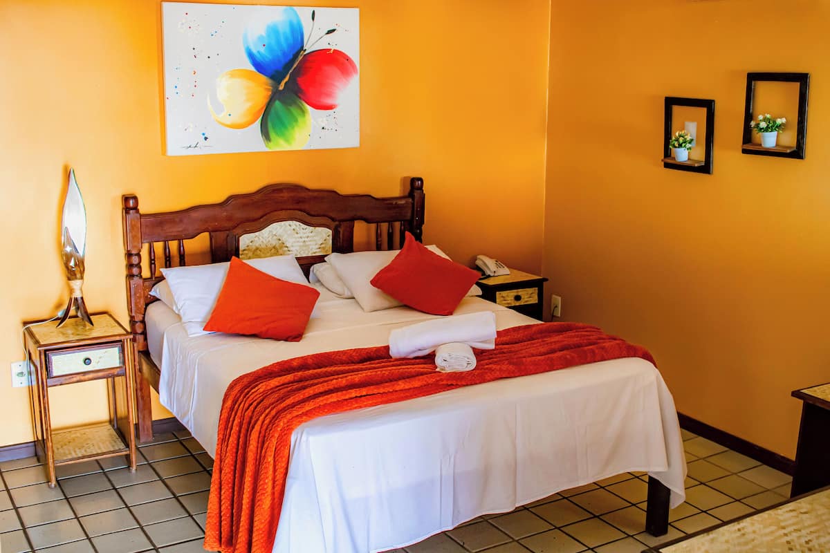 A neatly made bed with white linens and red pillows, a wooden headboard, and a red throw blanket.