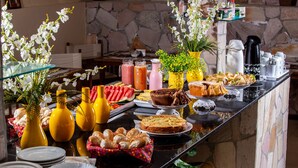 Ein reichhaltiges Buffet mit verschiedenen Speisen, darunter Brot, Gebäck und Kuchen, sowie mehrere Getränkespender und dekorative Blumen.