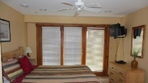 Ein Schlafzimmer mit Bett, Schminktisch, Deckenventilator und einem Fenster mit Jalousien.