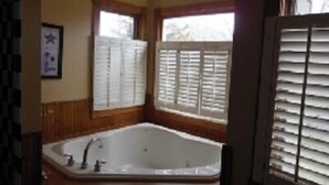 Ein Badezimmer mit einer großen Badewanne, Holzwänden und einem Fenster mit Rollläden.