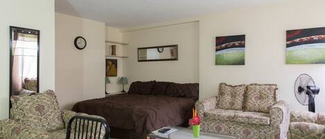A living room with a bed, two patterned sofas, a coffee table, a clock, and a fan.