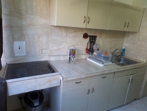 A kitchen with beige cabinets, a sink, and a dish rack. - Island Breeze Studio (Ocho Rios)