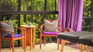 A room with two wooden chairs, one with a purple cushion and another with a grey cushion, a small round table with a bowl and a plant, and a large window with a view of greenery. - Hotel Isla Verde (Boquete)