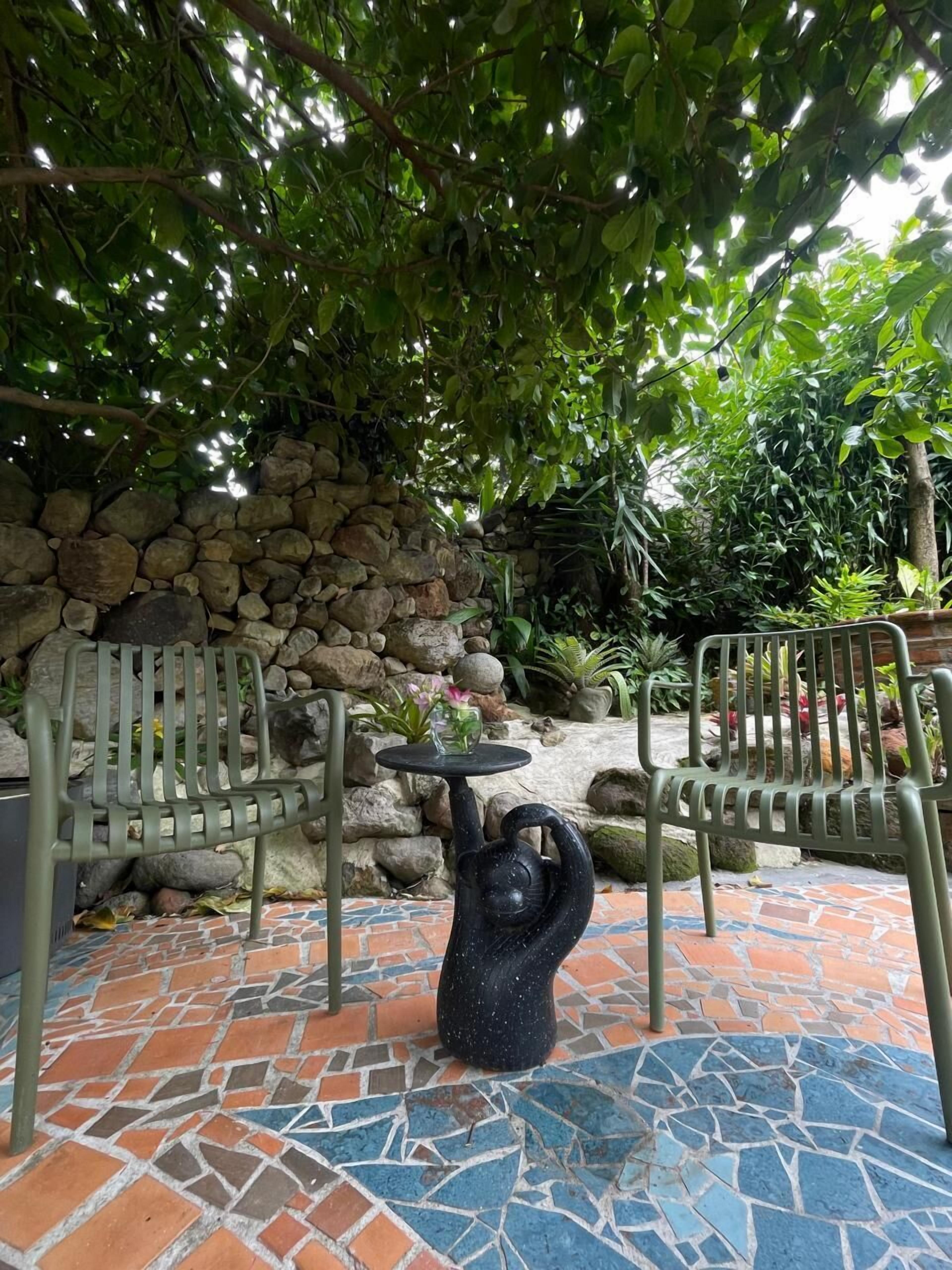 A patio with stone walls, two metal chairs, a decorative sculpture, and a tiled floor.