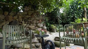 A patio with stone walls, two metal chairs, a decorative sculpture, and a tiled floor.