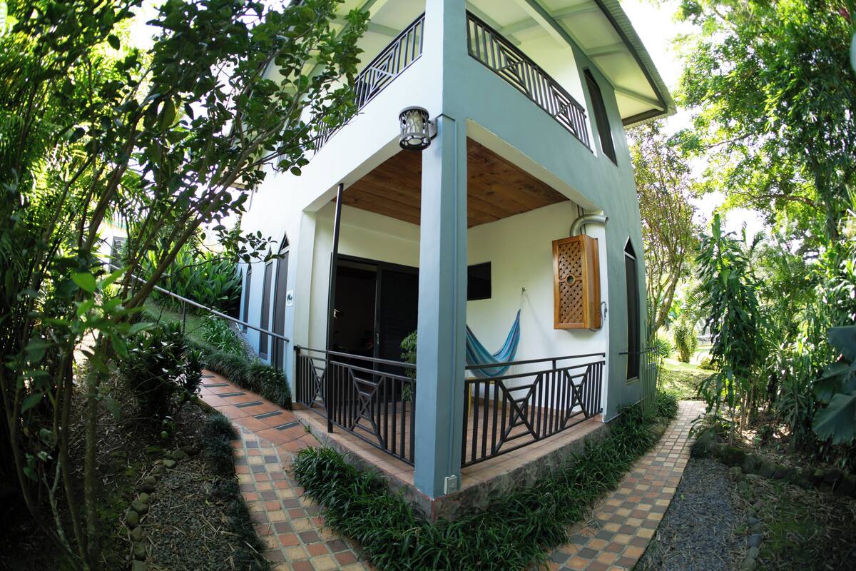 A two-story house with a balcony, a hammock, and a garden path.